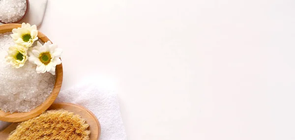 Spa yassı kompozisyonu. Deniz tuzu, banyo havlusu, masaj ahşap fırçası, beyaz arka planda çiçek. Kopyalama alanı, üst görünüm. Evde bakım kavramı, rahatla ve dinlen..