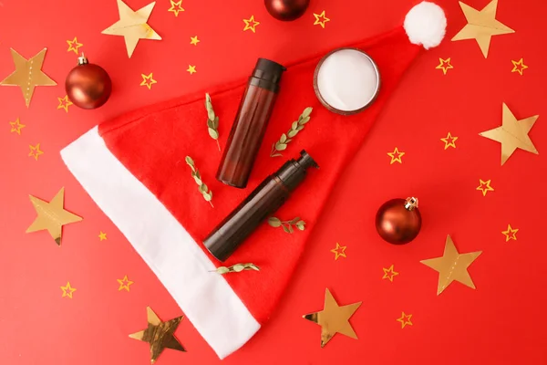 Kremalı yassı beste, kırmızı arka planda losyon esprisi Noel Baba şapkası. Güzellik kavramı, noel hediyesi, tatil atmosferi, yeni yıl, kutlama, doğal kozmetik ürünü, üst görünüm, kopyalanma alanı.