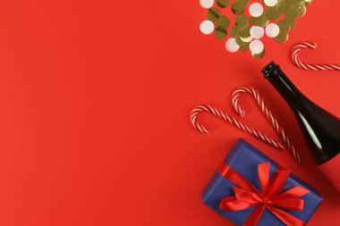 Şampanya şişesi ve kırmızı arka planda konfeti ile süsleme. Tatil atmosferi, yeni yıl kutlamaları, tebrik kartları. Düz çizgi, üst görünüm, çerçeve, kopyalanma alanı.
