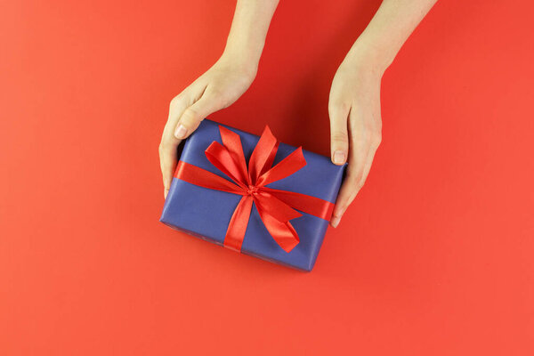 Hands hold christmas gift on red background. Concept holiday atmosphere, new year, celebration, greeting card. Flatlay, top view.