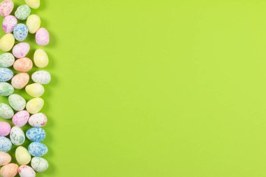 Mutlu Paskalyalar tatili konseptinin düz kompozisyonu. Yeşil arka planda renkli pastel yumurta. Üst görünüm, kopyalama alanı.