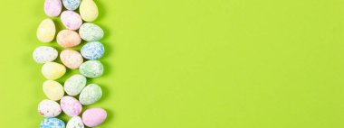 Mutlu Paskalyalar tatili konseptinin düz kompozisyonu. Yeşil arka planda renkli pastel yumurta. Üst görünüm, telif alanı, afiş.