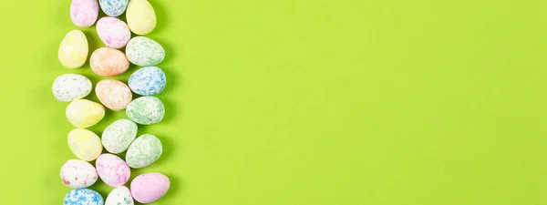 Mutlu Paskalyalar tatili konseptinin düz kompozisyonu. Yeşil arka planda renkli pastel yumurta. Üst görünüm, telif alanı, afiş.