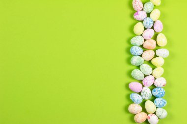 Mutlu Paskalyalar tatili konseptinin düz kompozisyonu. Yeşil arka planda renkli pastel yumurta. Üst görünüm, kopyalama alanı.