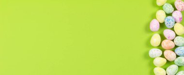 Mutlu Paskalyalar tatili konseptinin düz kompozisyonu. Yeşil arka planda renkli pastel yumurta. Üst görünüm, telif alanı, afiş.