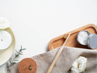 Doğal macun ve bej pamuk havluyla bambu diş fırçası, beyaz arka planda küçük bitki, yaprak, mum, çiçek. Çevre dostu kavramı, kopyalama, sıfır atık.