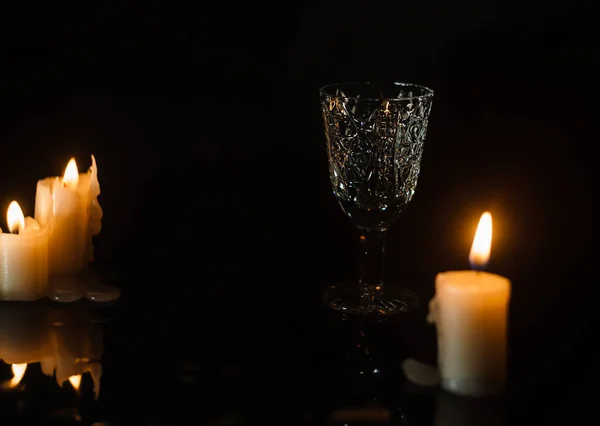 三支燃烧的蜡烛之间的黑色桌子上的一个水晶玻璃杯 带有复制空间 — 图库照片