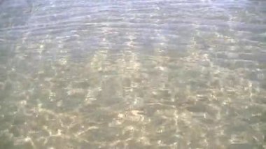 Güneşli bir günde sığ bir suda, kumlu bir zeminde bir ışık dalgası var ve parlak güneşin parlaklığı yansıyor.