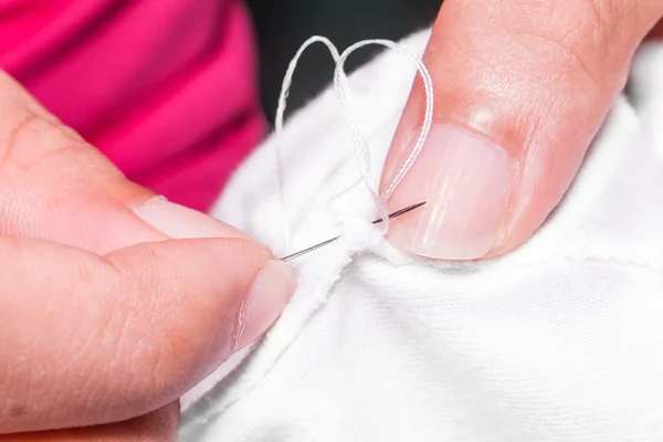 Женские руки при шитье белой ткани — стоковое фото
