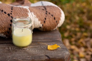 Bankada, parktaki ahşap bankta örülmüş giysiler ve mum. Sonbahar Yünlü Süveteri.