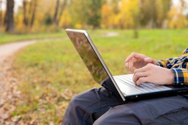 Adam parkta oturuyor ve dışarıda dizüstü bilgisayarda çalışıyor. Klavyede yazan eller.