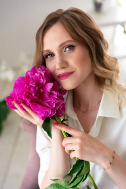 Kadın gömlekli, elinde şakayık buketi, kameraya bakıyor ve gülümsüyor. Güzel sarışın kadın portresi. Randevu için sürpriz bir buket çiçek, anneler günü ya da sevgililer günü