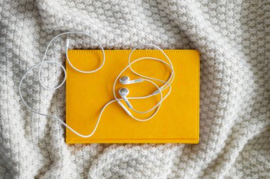 Sarı bir not defterinde beyaz kulaklıklar var. Gri örülmüş arka plan. Ev ödevi. Uzaklık eğitimi