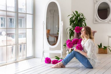 Gömlekli ve kotlu bir kadın elinde şakayık buketi tutuyor. Güzel sarışın kadın portresi. Randevu için sürpriz bir buket çiçek, anneler günü ya da sevgililer günü