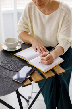 İş kadını elinde akıllı telefonu tutuyor ve not defterine yazılar yazıyor. Günlük ya da haftalık iş planlama ve görevler. İş hayatında bir kadın