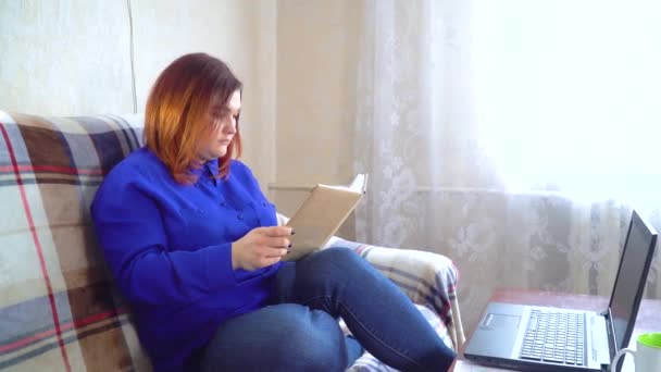 Jonge Kaukasische vrouw zit op de bank en leest een boek thuis — Stockvideo