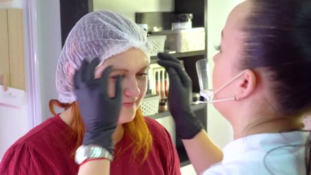 Maquillaje artista se pone una gorra en la mujer joven antes de aplicar el maquillaje — Vídeo de stock