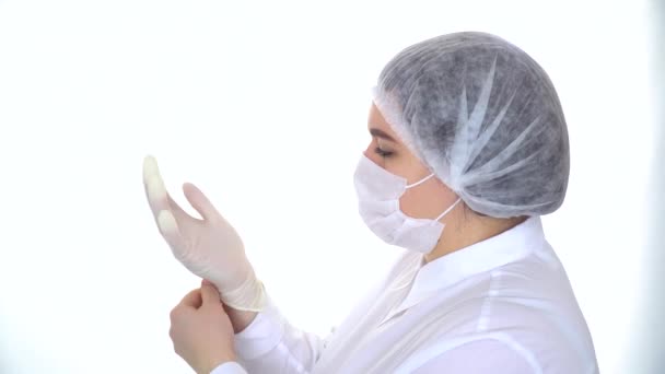 Jovem médica caucasiana em máscara protetora e boné colocando luva protetora branca. Conceito médico e de saúde — Vídeo de Stock