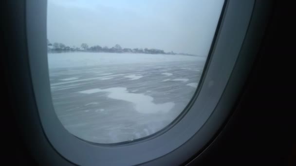 Utsikt från det rörliga flygplansfönstret på startlandningsbanan på den snöiga flygplatsen — Stockvideo