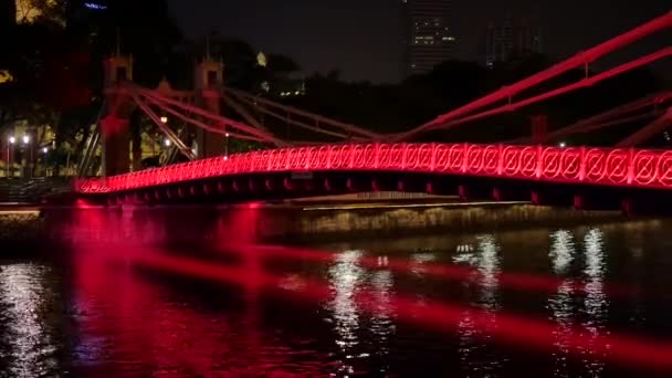 Toeristische boot beweegt onder de rode verlichte brug in de avond in Singapore — Stockvideo