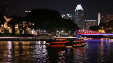 Singapur 'daki Fullerton Oteli' ni aydınlattı ve tekneler köprüye yaklaşıyor.