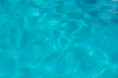 Işık açık mavi havuz suyunda dans eder. Yüzey dalgalanır ve dinlendirici bir tatil sırasında parlak güneşi yansıtır..