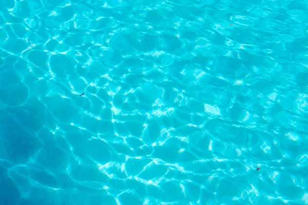 Temiz turkuaz su, yüzme havuzundaki güneş ışığını yansıtır. Ferahlatıcı suyun soyut bir görüntüsü, yaz tatili geçmişi.