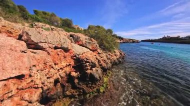 PORTOCOLOM, MALLORCA, İSPA - 25 EKİM 2025: Deniz kayalık kıyıya hafifçe döner, Mallorca 'da dinlendirici bir günde güneş parlar. Geniş açı. Ağır çekim için kullanılabilir..