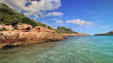 PORTOCOLOM, MALLORCA, İSPAN 22 EKİM 2025: dalgalar kayalık kıyıya çarpar. Güzel turkuaz su ve mavi gökyüzü Mallorca 'da rahatlatıcı bir yaz atmosferi yaratıyor..