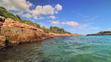 PORTOCOLOM, MALLORCA, İSPAN - 22 Ekim 2025 Akdeniz 'de rahatlatıcı bir gün. Sakin turkuaz su, güneşli bir gökyüzünün altında kayalık kıyı şeridine hafifçe dalgalanıyor..