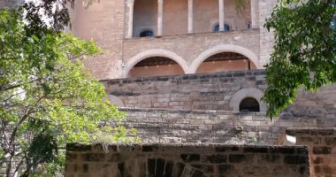 Palma Mayorka İspanya 'daki antik Almudaina Sarayı' nın detaylı manzarası. Güneş ışığı, taş cephesini ve yeşil ağaçları aydınlatır..