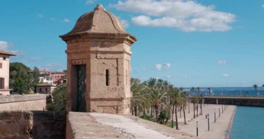 Mayorka, Palma 'daki Almudaina Sarayı surlarından görüntü. Güneşli liman güvertesi ve mavi denizin yanında tarihi bir muhafız kulübesi duruyor..