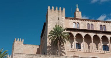 İspanya 'nın Palma de Mallorca şehrinde Almudaina Kraliyet Sarayı parlak mavi bir gökyüzünün altında duruyor. Açık bir günde palmiye ağaçlarıyla tarihi mimari.