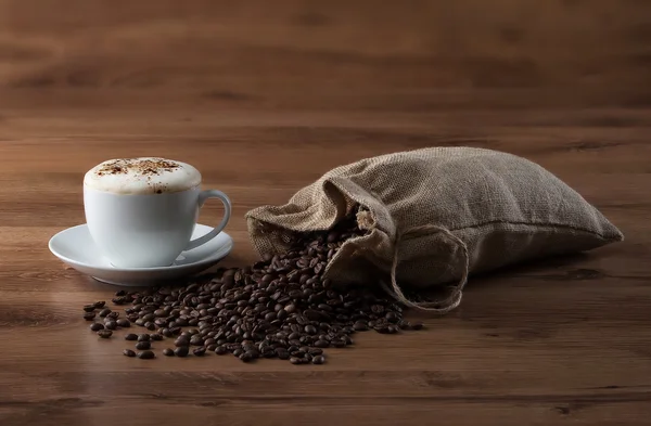 Koffiekopje en tas met bonen op houten textuur — Stockfoto