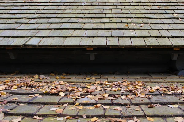 Layered roof made of wooden shingles. Shingle roof covered with dry leaves.