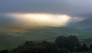 Bulutların arasından geçen bir parça güneş ışığı dağın eteklerindeki tepelerde