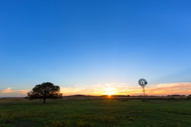 The sun, a windmill and a lone tree clipart