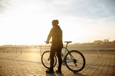 Bisikletli siyah elbiseli ve kasklı trenlerde bisiklet sürüyor.