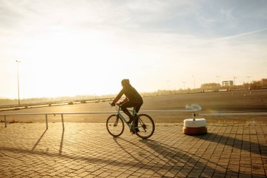 Bisikletli siyah elbiseli ve kasklı trenlerde bisiklet sürüyor.