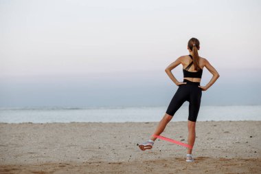 Güzel spor kızı deniz kenarında lastik bantlarla spor yapıyor.