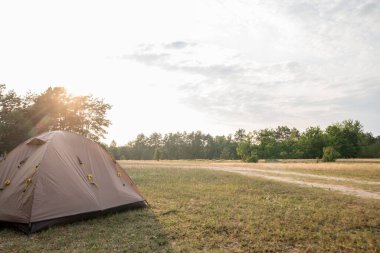 Kahverengi çadır günbatımının arka planında çimlerin üzerinde duruyor.