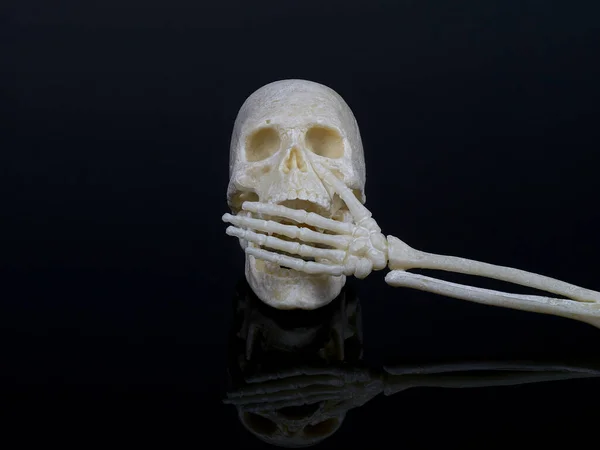 Human skull covers its mouth with a skeleton hand, cannot speak, sign of silence or violence — Stockfoto