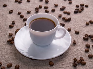 Beyaz bir espresso fincanı kahve çekirdekleri ile bir çuval masasında duruyor.