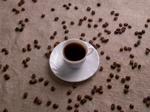 Beyaz bir espresso fincanı kahve çekirdekleri ile bir çuval masasında duruyor.