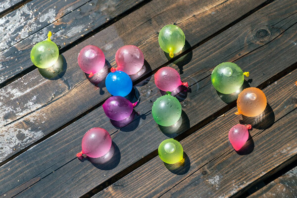 colored inflatable rubber balls for throwing each other, as children's fun. filled with water and lying on a wooden background.
