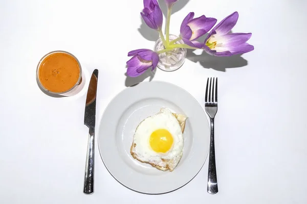 白い背景に隔離されたおいしい朝食 トーストのスクランブルエッグ ナイフとフォーク 新鮮な絞りたてのニンジンジュースと花瓶のクルーズの花束 — ストック写真