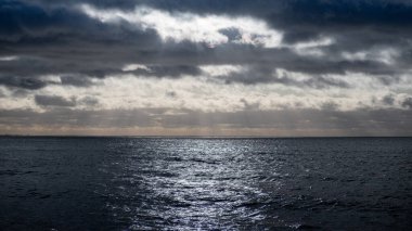 Denizde güzel bir gün batımı, bulutların arasından düşen ve sudan yansıyan güneşin izi..