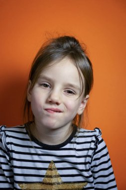 Yüzünde şüphe ve belirsizlik duygusu olan yemyeşil lavların arka planında küçük güzel bir kız. Güzel saçlı güzel bir kız uzun kollu çizgili bir tişörtün içinde bir şeyden şüpheleniyor..