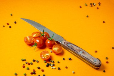 Yemek geçmişi. Bir dalda taze kırmızı vişneli domates ya da tatlı bir kız, farklı çeşitte biber ve renkli sarı arka planda bir bıçak, yatay yönelim