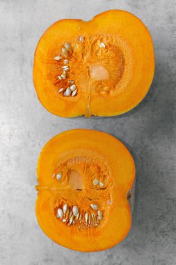 Bir balkabağının iki yarısı gri arka planda ikiye bölünmüş, çekirdek, hamuru ve kabak çekirdeği.